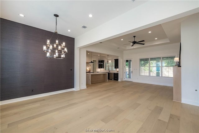 unfurnished living room with ceiling fan with notable chandelier, light hardwood / wood-style floors, and a raised ceiling