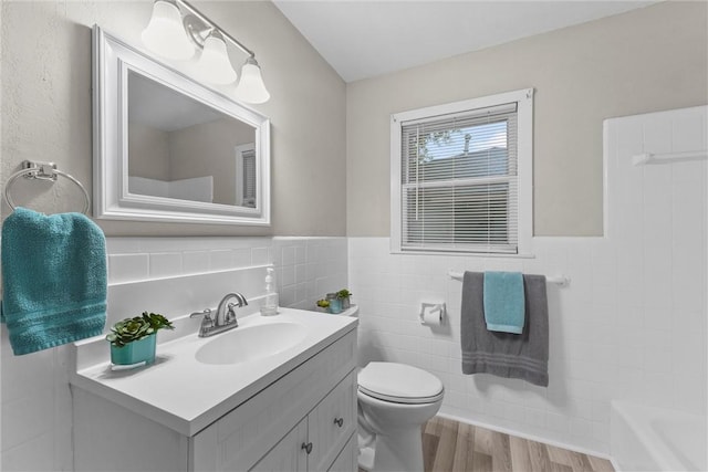 907 Barnhill St, Brenham, TX 77833 - full bathroom featuring tile walls, vanity, a tub to relax in, wood finished floors, and a wainscoted wall