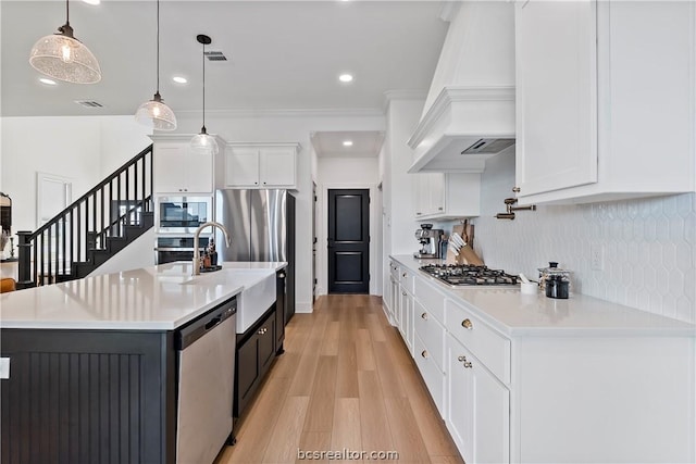 kitchen with appliances with stainless steel finishes, premium range hood, pendant lighting, light hardwood / wood-style flooring, and white cabinetry