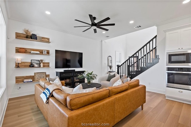 living room featuring ceiling fan, ornamental molding, a fireplace, and light hardwood / wood-style flooring