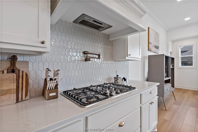 kitchen with light wood-type flooring, backsplash, ornamental molding, stainless steel gas cooktop, and white cabinetry