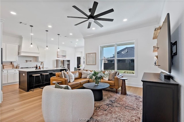 living room with ceiling fan, sink, light wood-type flooring, and crown molding