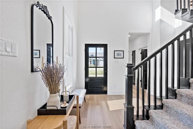 foyer entrance with a towering ceiling and light wood-type flooring