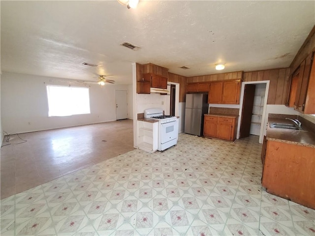 kitchen featuring a textured ceiling, ceiling fan, sink, stainless steel refrigerator, and white gas stove