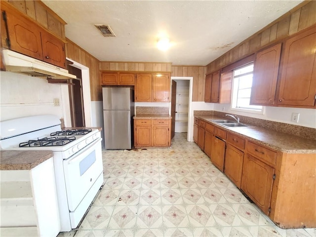 kitchen with stainless steel fridge, wooden walls, gas range gas stove, and sink