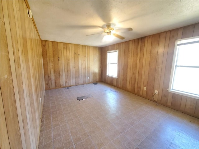 unfurnished room with wood walls, ceiling fan, and a healthy amount of sunlight