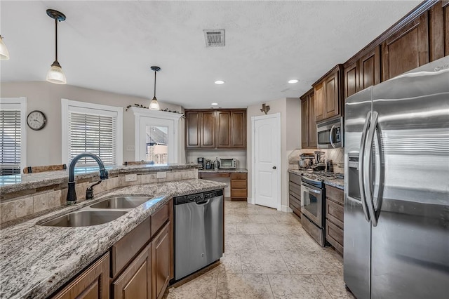 kitchen with light stone counters, visible vents, a sink, hanging light fixtures, and stainless steel appliances