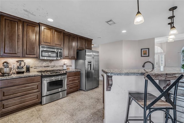 kitchen featuring visible vents, appliances with stainless steel finishes, pendant lighting, a kitchen bar, and tasteful backsplash