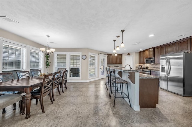 kitchen with visible vents, a breakfast bar area, stone countertops, stainless steel appliances, and a kitchen island with sink