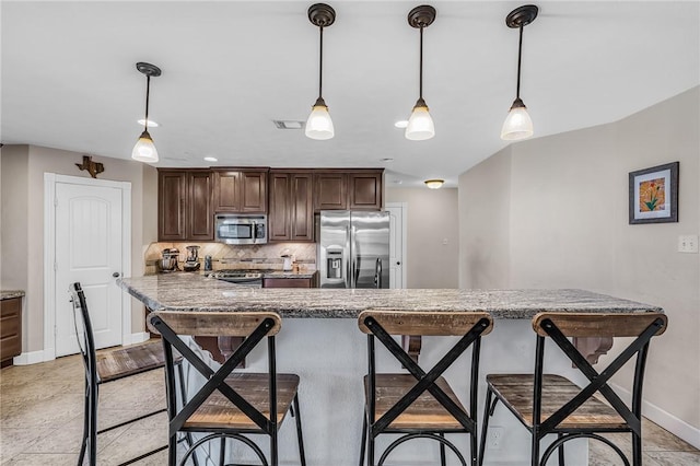 kitchen with a breakfast bar, decorative backsplash, dark brown cabinetry, appliances with stainless steel finishes, and pendant lighting