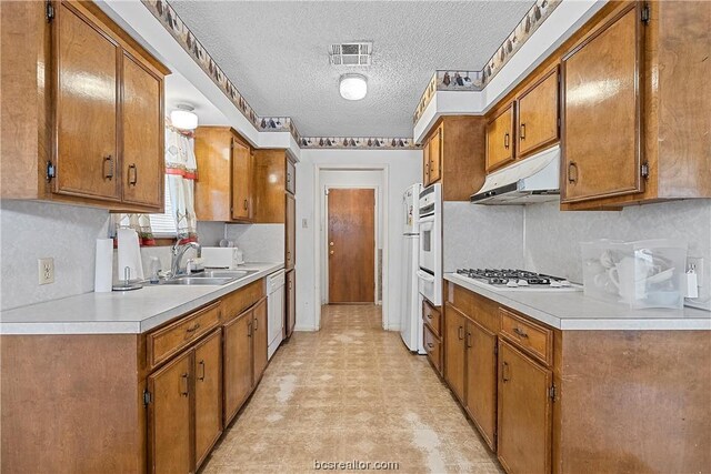 kitchen with a textured ceiling, white appliances, and sink