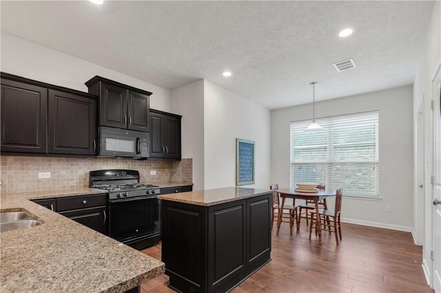 kitchen featuring pendant lighting, tasteful backsplash, hardwood / wood-style flooring, a center island, and black appliances