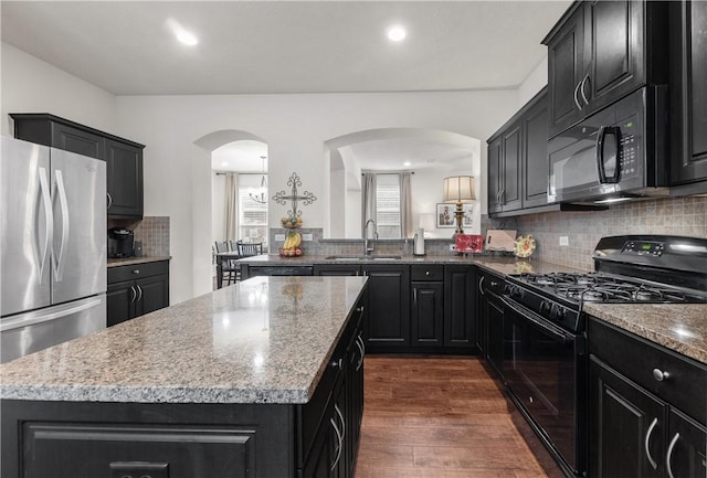 kitchen with dark wood-type flooring, sink, light stone counters, a kitchen island, and black appliances