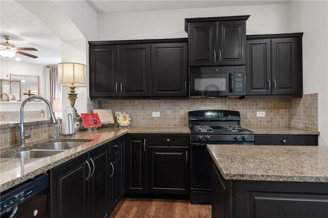 kitchen with sink, backsplash, dark hardwood / wood-style floors, light stone counters, and black appliances