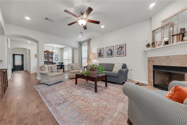 living room with ceiling fan with notable chandelier, light hardwood / wood-style floors, and a tile fireplace