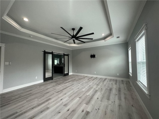 unfurnished bedroom featuring a barn door, a raised ceiling, light hardwood / wood-style floors, and ornamental molding