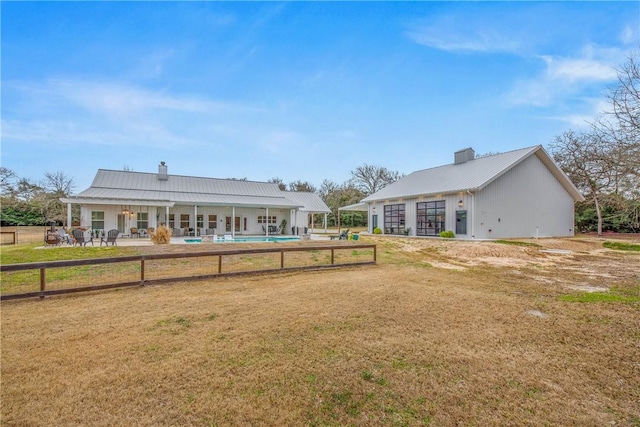 rear view of house featuring a fenced in pool, metal roof, a chimney, and a patio