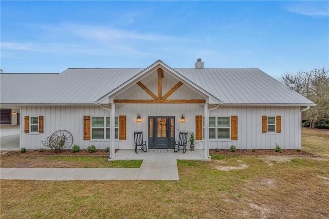 view of front of home with board and batten siding, a front yard, metal roof, and a chimney