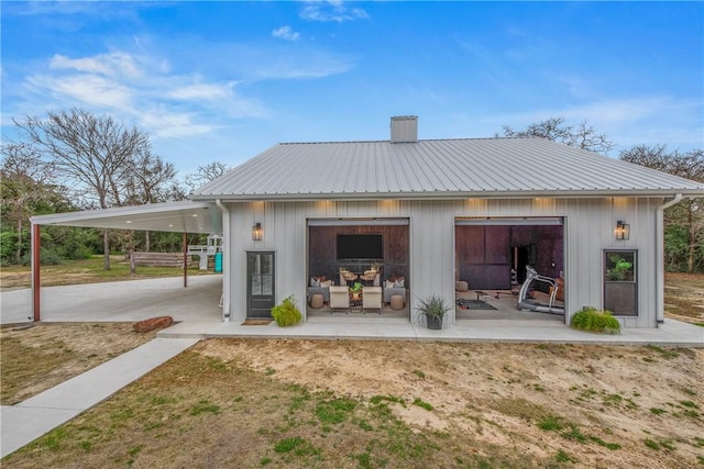 rear view of house with a garage, metal roof, a chimney, and a patio