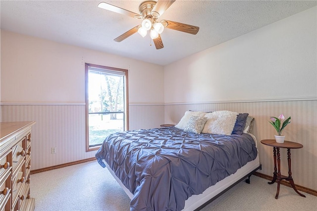 bedroom with ceiling fan, light colored carpet, and a textured ceiling