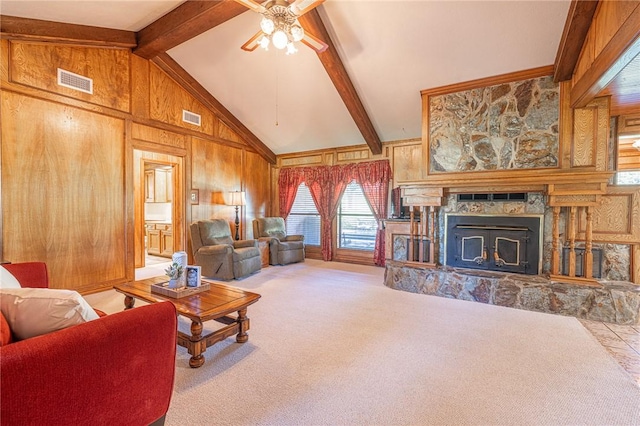 living room with carpet, wood walls, a stone fireplace, ceiling fan, and beamed ceiling