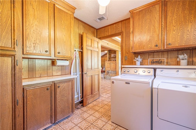 clothes washing area featuring cabinets, a textured ceiling, ceiling fan, wooden walls, and washing machine and clothes dryer