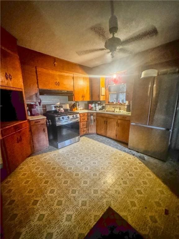 901 Post Oak St, Hearne, TX 77859 - kitchen with stainless steel gas range, a ceiling fan, brown cabinetry, under cabinet range hood, and light countertops