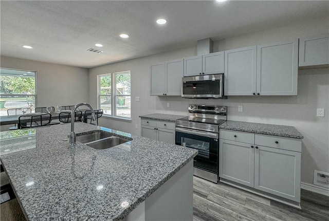 kitchen featuring an island with sink, light stone counters, stainless steel appliances, and a sink