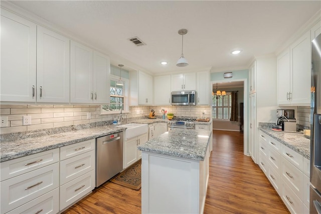 kitchen with a kitchen island, appliances with stainless steel finishes, pendant lighting, white cabinetry, and sink