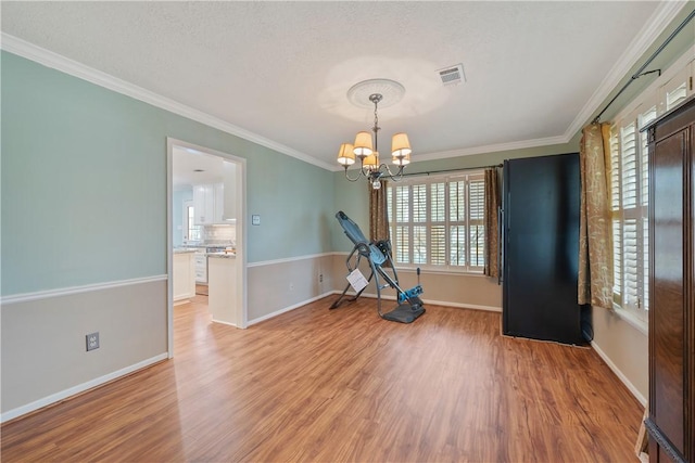 exercise room with crown molding, an inviting chandelier, and light hardwood / wood-style floors