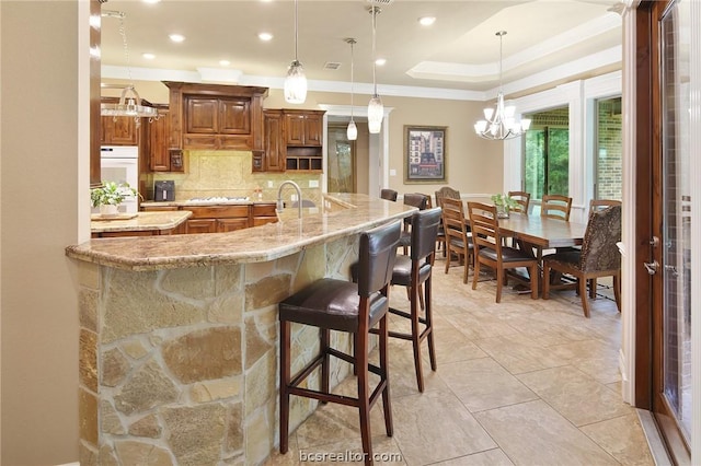 kitchen with tasteful backsplash, light stone counters, a breakfast bar, an inviting chandelier, and hanging light fixtures