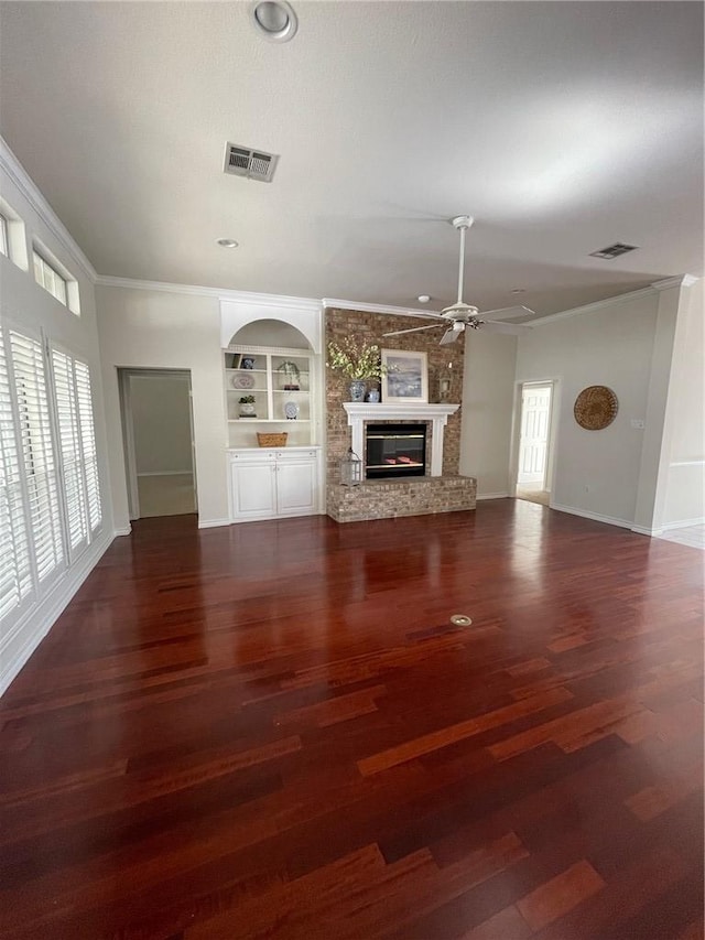 unfurnished living room featuring built in shelves, a large fireplace, dark hardwood / wood-style floors, ornamental molding, and ceiling fan