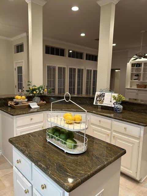 kitchen with light tile patterned flooring, ornamental molding, dark stone counters, a kitchen island, and white cabinets