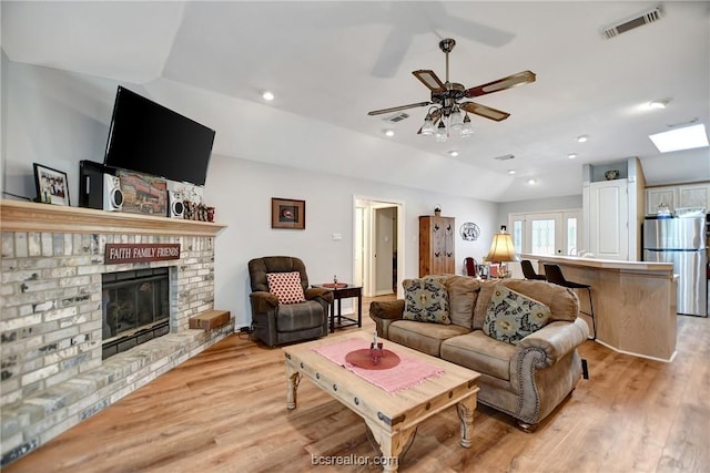 living room with a fireplace, light hardwood / wood-style floors, vaulted ceiling, and ceiling fan