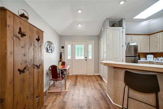 kitchen with lofted ceiling with skylight, sink, light hardwood / wood-style flooring, a kitchen bar, and stainless steel refrigerator