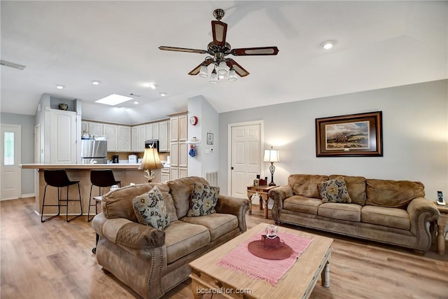 living room featuring light hardwood / wood-style flooring, ceiling fan, and lofted ceiling with skylight