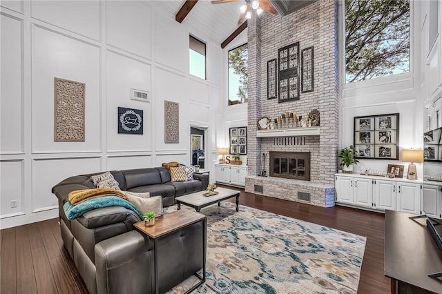 living room featuring beam ceiling, ceiling fan, dark wood-type flooring, a brick fireplace, and high vaulted ceiling