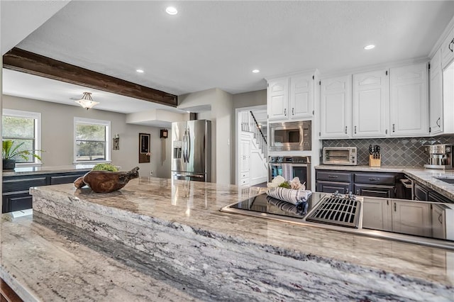 kitchen with appliances with stainless steel finishes, tasteful backsplash, light stone counters, beamed ceiling, and white cabinetry