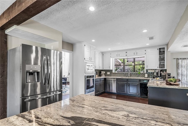 kitchen with stainless steel appliances, white cabinetry, tasteful backsplash, and light stone counters