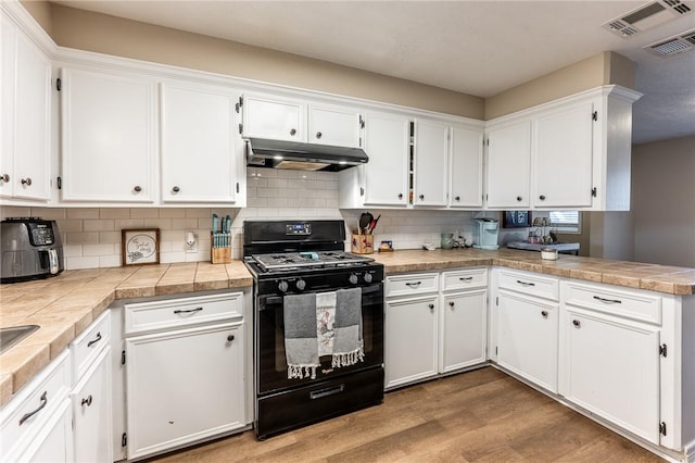 kitchen featuring tile countertops, black range oven, decorative backsplash, light wood-type flooring, and white cabinetry