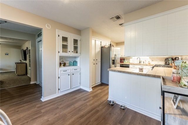 kitchen featuring kitchen peninsula, stainless steel fridge, tasteful backsplash, dark wood-type flooring, and white cabinetry