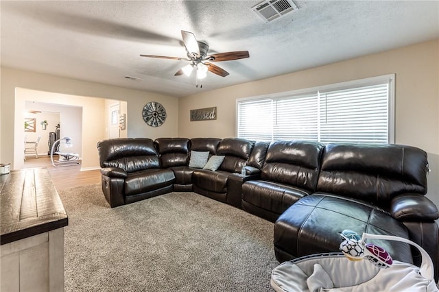 living room with ceiling fan, light colored carpet, and a textured ceiling