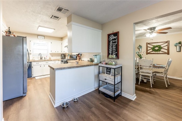 kitchen with dark wood-type flooring, kitchen peninsula, a textured ceiling, white cabinets, and appliances with stainless steel finishes