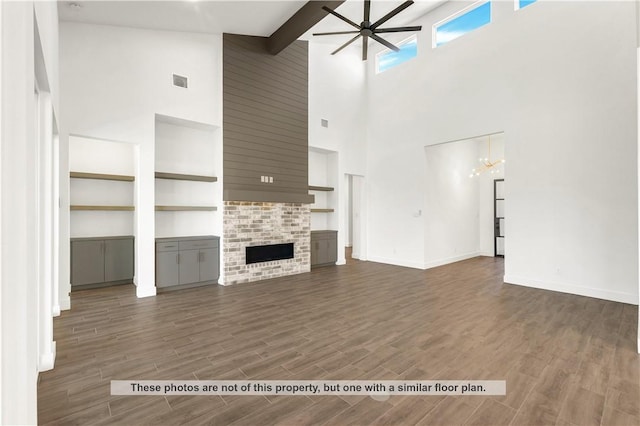 unfurnished living room with ceiling fan with notable chandelier, dark hardwood / wood-style floors, high vaulted ceiling, and a brick fireplace