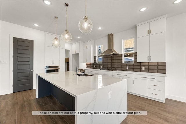 kitchen featuring a large island with sink, white cabinetry, stainless steel oven, and wall chimney exhaust hood