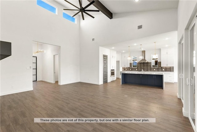 unfurnished living room with dark hardwood / wood-style flooring, ceiling fan with notable chandelier, sink, beam ceiling, and high vaulted ceiling