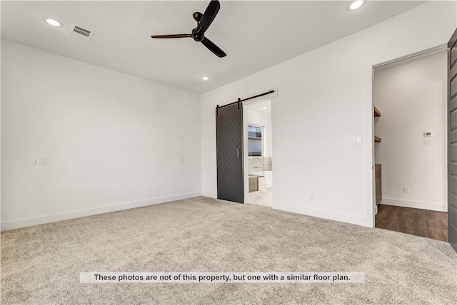 carpeted spare room with a barn door and ceiling fan