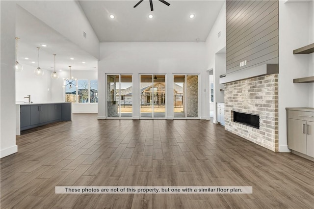 unfurnished living room featuring dark wood-type flooring, high vaulted ceiling, sink, ceiling fan, and a fireplace