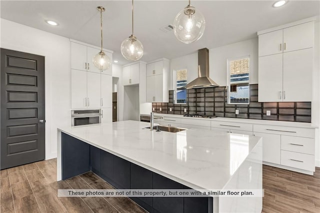 kitchen featuring white cabinetry, a large island, wall chimney exhaust hood, pendant lighting, and wood-type flooring