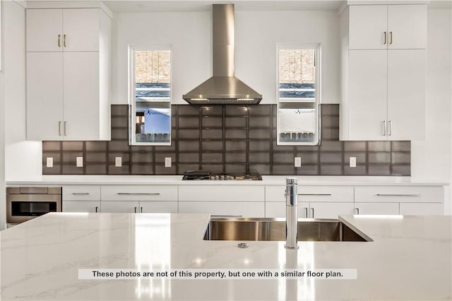 kitchen featuring decorative backsplash, light stone counters, stainless steel appliances, and wall chimney range hood